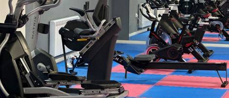 Un gimnasio con varias máquinas de ejercicio, incluyendo cintas de correr y bicicletas estáticas, dispuestas en filas.