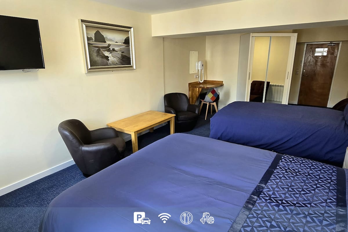 A hotel room with two beds, a desk, a chair, a TV, and a painting on the wall.