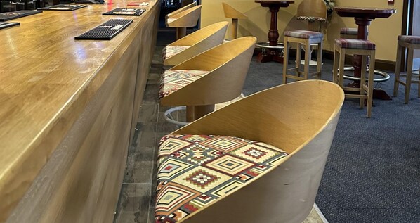 Angolo bar con un bancone in legno e diversi sgabelli da bar con cuscini decorati.