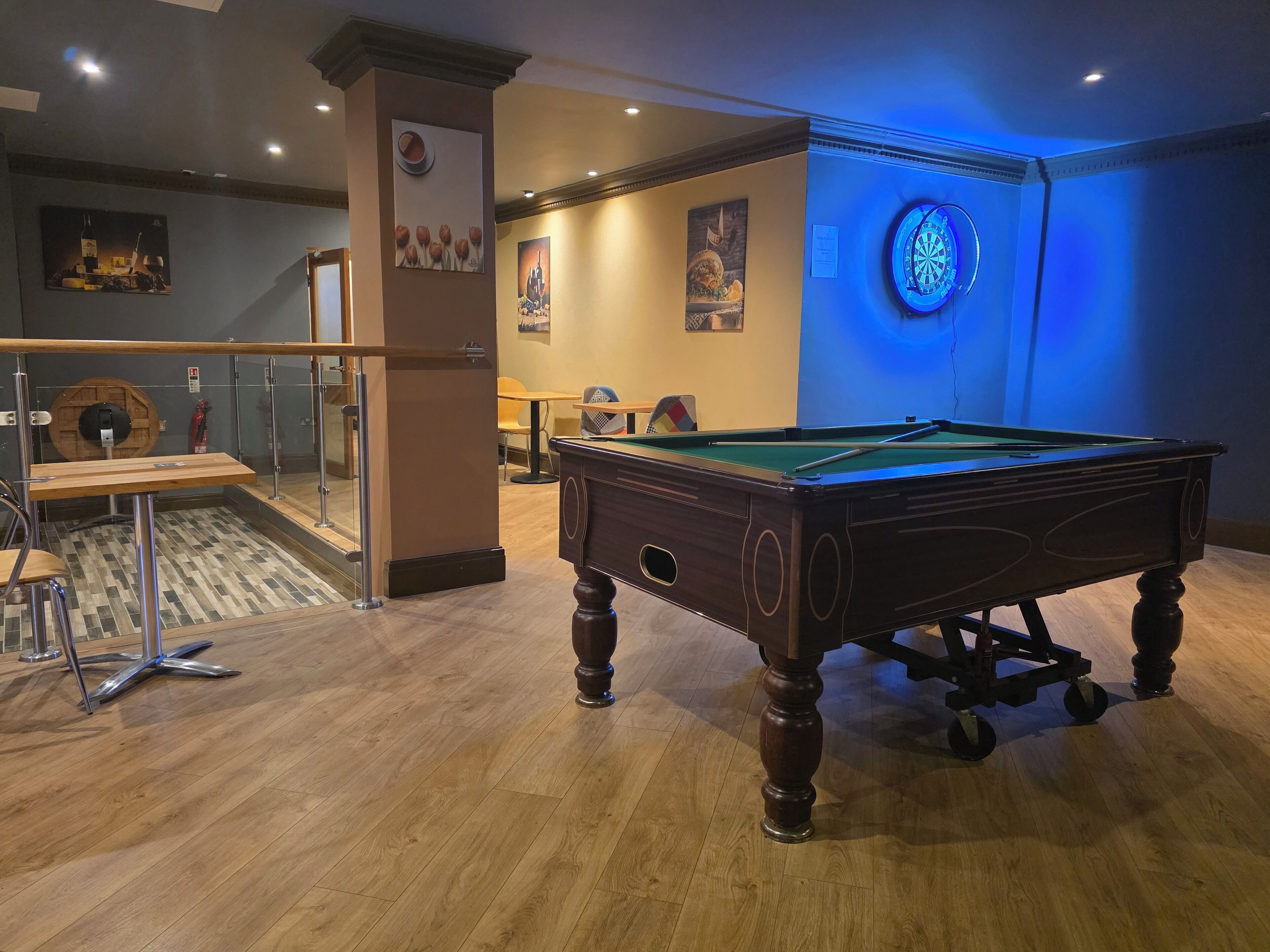 A pool table in a room with wooden flooring, a glass partition, and a blue neon light.