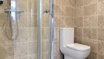 A modern bathroom with a glass-enclosed shower, a white toilet, and beige tiled walls.