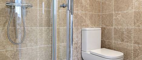 A modern bathroom with a glass-enclosed shower, a white toilet, and beige tiled walls.
