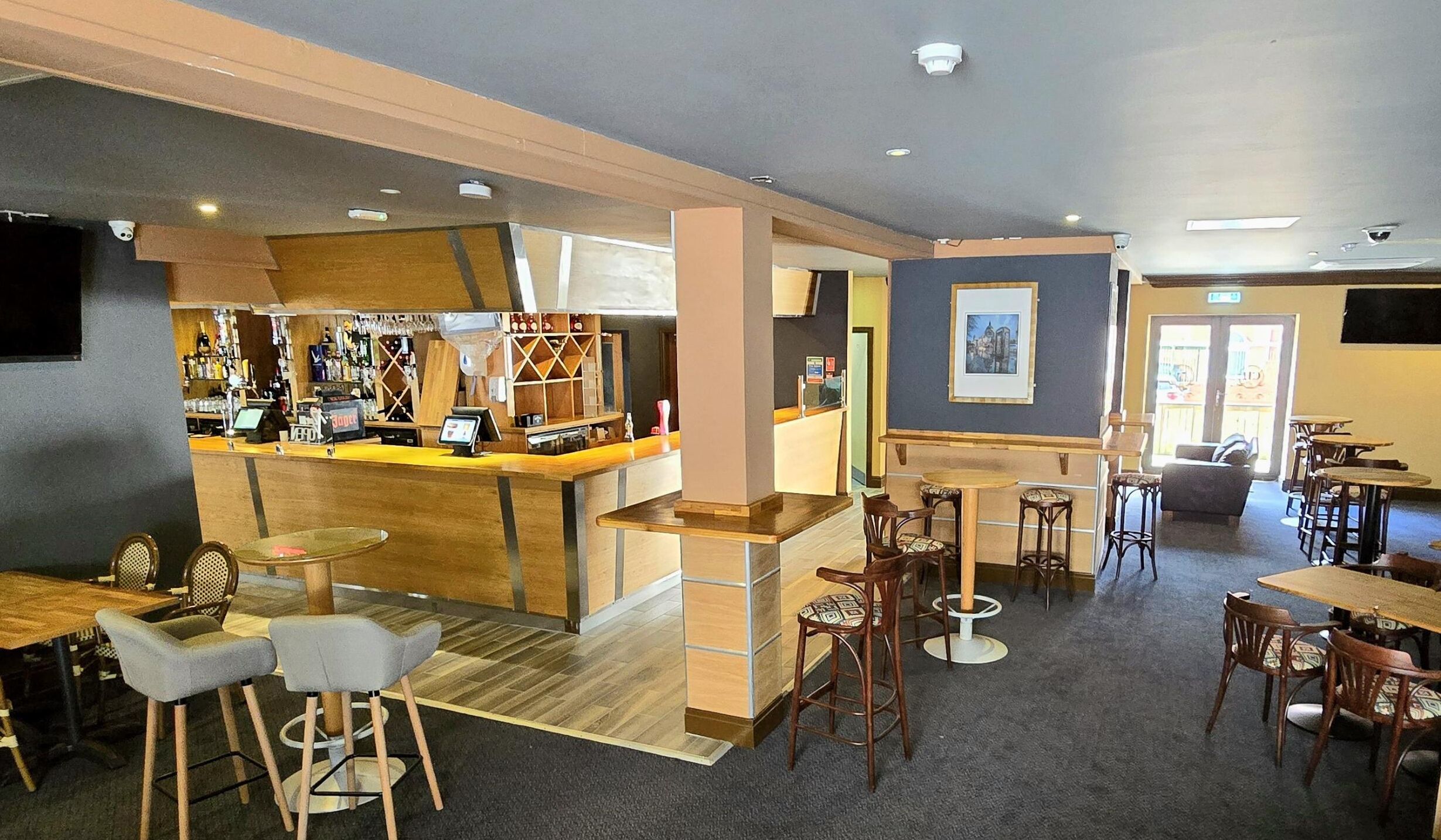 A restaurant with a bar area, multiple seating options including bar stools and tables, and a counter with a cash register.