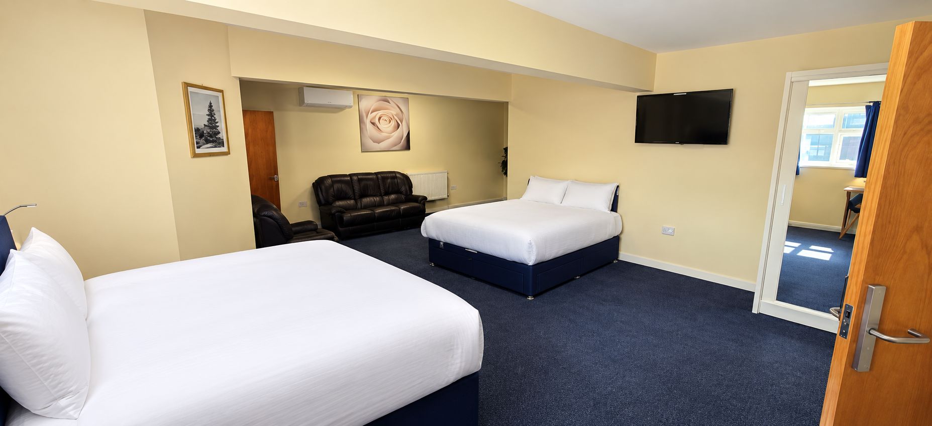 A hotel room with two beds, a sofa, a TV, and a door leading to another room.