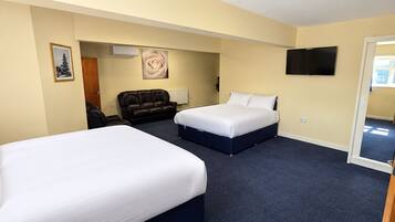 Een hotelkamer met twee bedden, een bank, een televisie en een deur naar een andere kamer.