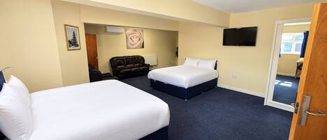 A hotel room with two beds, a sofa, a TV, and a door leading to another room.
