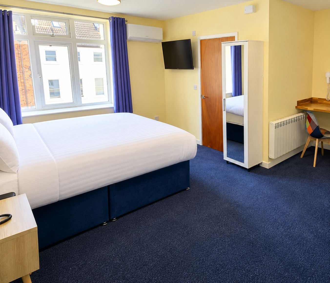 A hotel room with a bed, a desk, a chair, a television, and a door leading to another room.