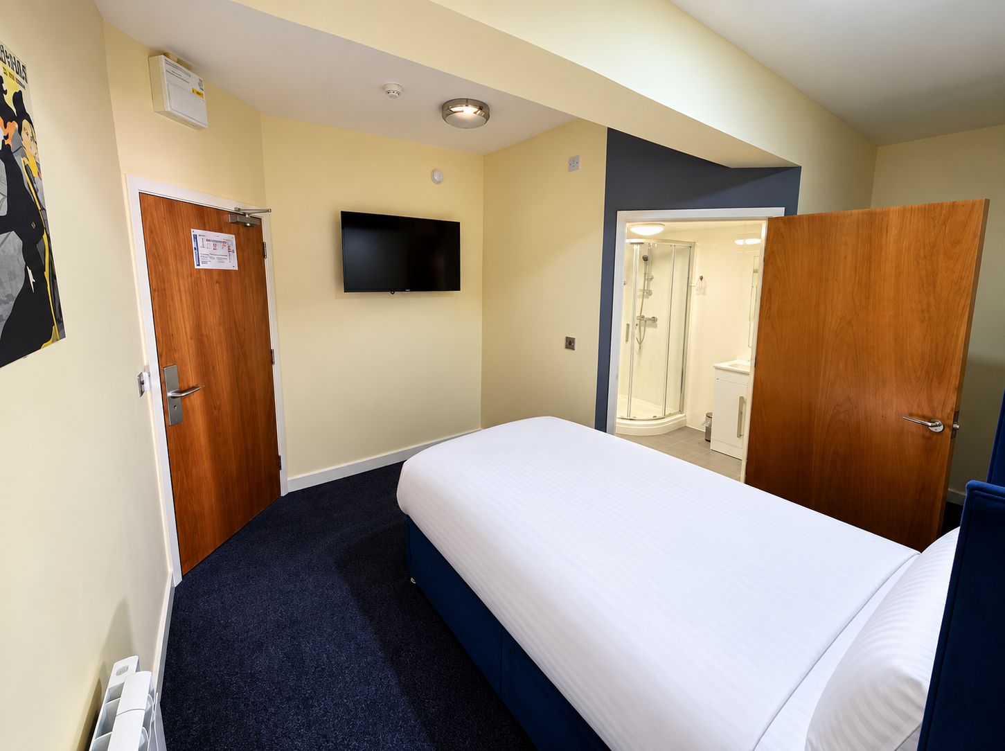 Una habitación de hotel con una cama, televisor, ducha y puerta.