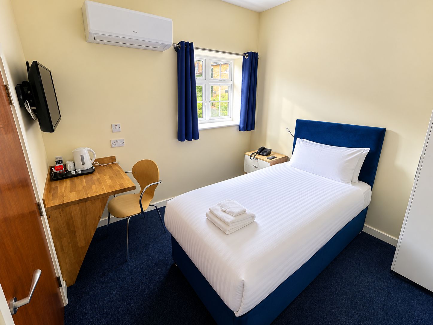 Ein Hotelzimmer mit einem Bett, einem Schreibtisch mit Stuhl, einem Telefon und einer Klimaanlage.