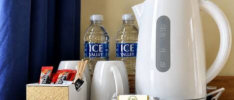 A hotel room's breakfast tray with a white coffee maker, two bottles of water, a tea bag holder, and a small sign for the Carmichael Hotel.