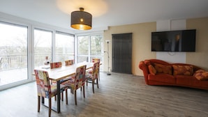 Ein modernes Wohnzimmer mit Essbereich, großen Fenstern, einem roten Sofa und einem wandmontierten Fernseher.