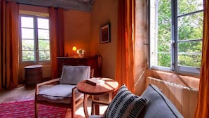 A cozy room with a sofa, two chairs, a small table, a lamp, and a window with curtains. - La Bastide du Farfadet (Laudun)