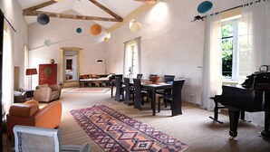 A spacious living room with a dining area, a piano, and a large window with curtains. - La Bastide du Farfadet (Laudun)