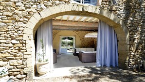 A stone building with a covered patio area featuring wicker furniture and a potted plant. - La Bastide du Farfadet (Laudun)