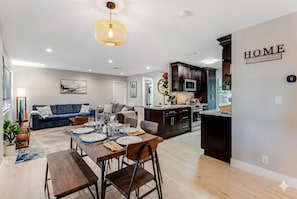 A modern living room with a dining area, kitchen, and a 'HOME' sign on the wall.
