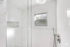 A modern bathroom with a glass shower enclosure, a frosted window, and a handheld showerhead.