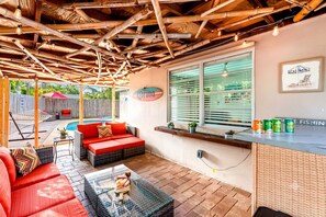 A covered outdoor seating area with a pool, a Corona sign, and a bar with fishing cans.