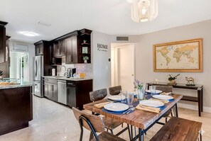 A modern kitchen with dark cabinetry, a marble countertop, and a dining area with a wooden table set for four.
