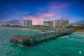 A pier extending into turquoise waters with buildings in the background.