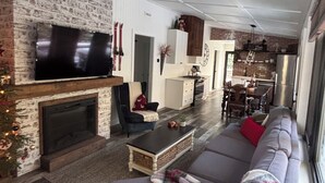 Una sala de estar moderna con chimenea, un televisor grande, un sofá y un comedor al fondo.