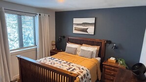 Un dormitorio con cama, mesita de noche, cómoda, ventana con persianas, lámpara de pared e imagen en la pared.