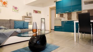 Ein modernes Wohnzimmer mit einem Glastisch, einer blauen Sofaecke und einer Küchenzeile mit Türkis-Schränken.