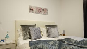 Ein ordentlich bezogenes Bett mit einer gemusterten Decke, ein Nachttisch mit Lampe und einem kleinen dekorativen Gegenstand, sowie eine Wand mit drei gerahmten Bildern.