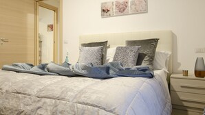 Ein ordentlich bezogenes Bett mit einem gemusterten Duvet und Kissen, ein Nachttisch mit einer Vase sowie eine Wand mit drei gerahmten Kunstwerken.