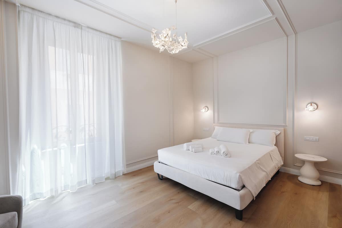 Een moderne slaapkamer met een groot bed, een kroonluchter en een nachtkastje.