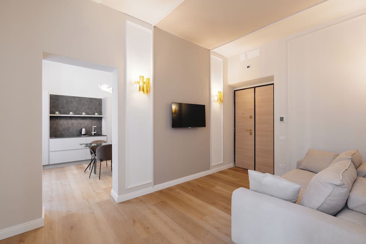 Een moderne woonkamer met een bank, een flatscreen televisie en een keukenhoek met een eettafel en stoelen.