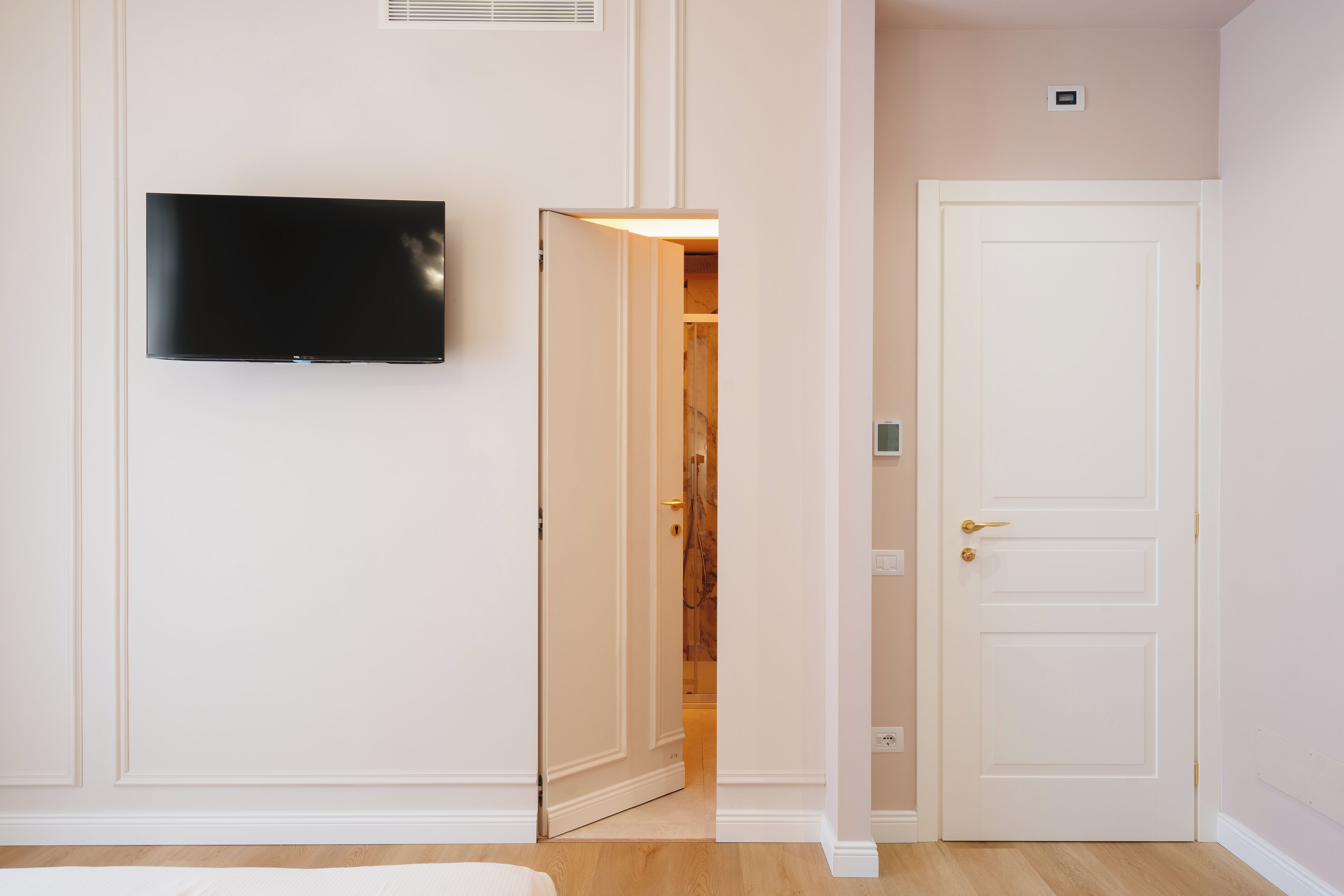 Una habitación con televisión de pantalla plana en la pared, una puerta blanca y un pasillo que conduce a otra habitación.