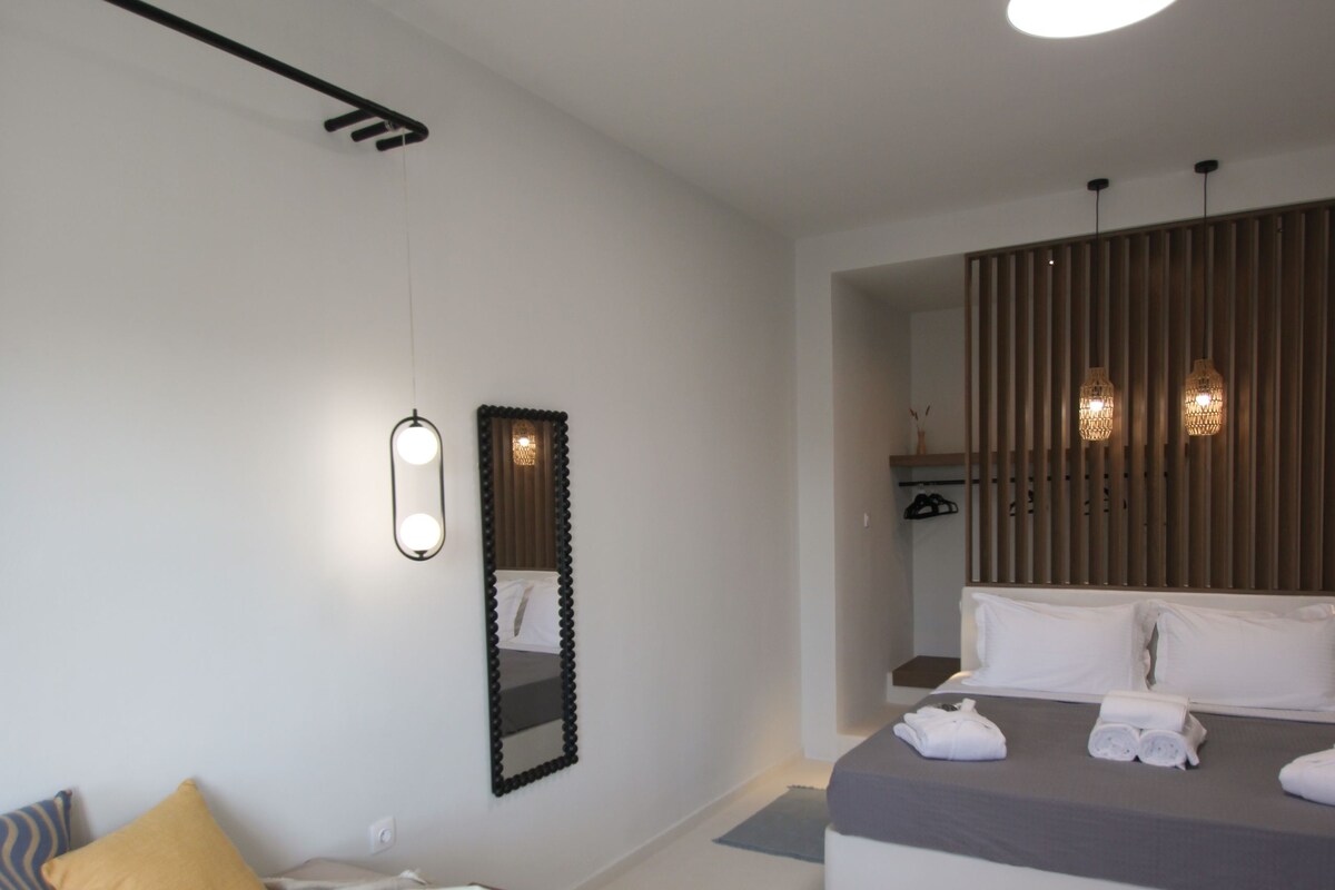 A modern hotel room with a bed, bedside table, and a bathroom with a sink and mirror.