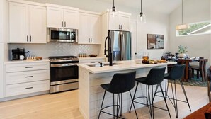 Een moderne keuken met witte kasten, roestvrijstalen apparatuur en een centraal keukenblok met barkrukken.