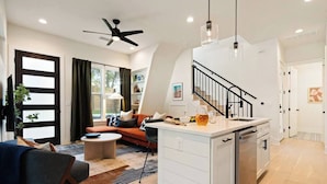 Een moderne keuken met een centraal eiland, een zithoek met een bank en een trap naar een hoger niveau.