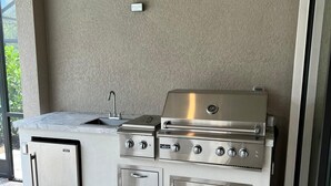 Eine Außenküche mit Grill aus Edelstahl, Spüle und Kühlschrank.