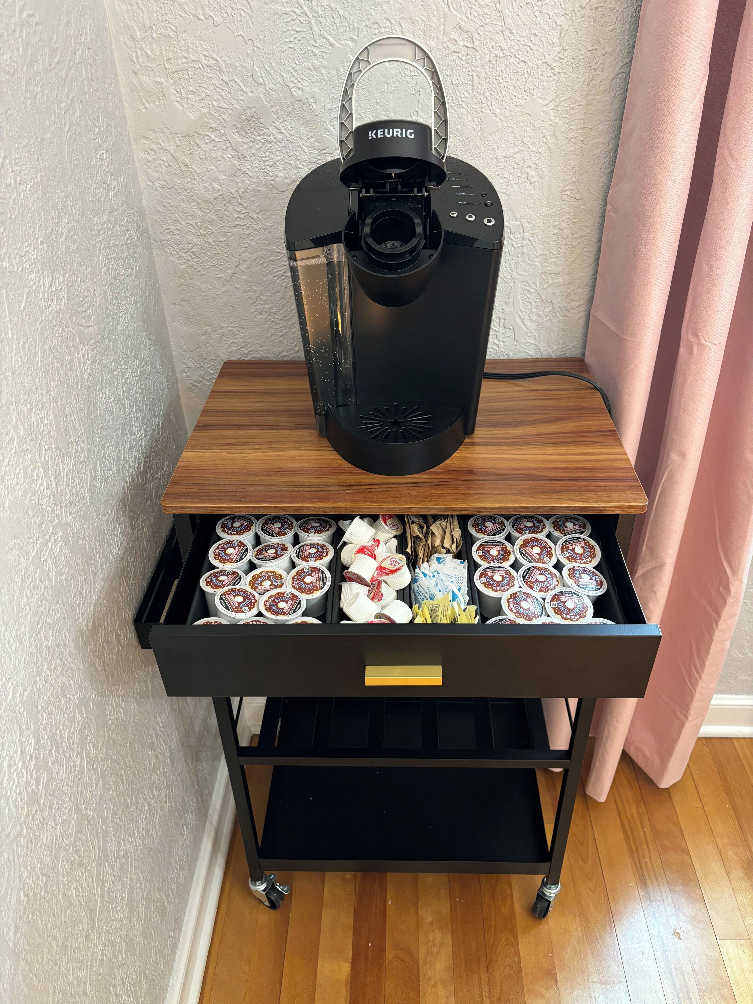 A Keurig coffee maker on a wooden shelf with a drawer below containing coffee pods.