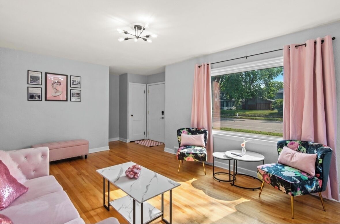 Una sala de estar moderna con un sofá, dos sillones, una mesita de centro y vista a una calle residencial.