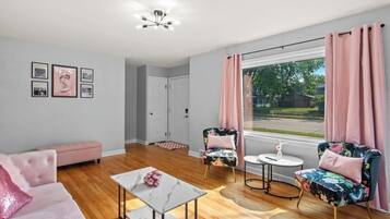 Una sala de estar moderna con un sofá, dos sillones, una mesita de centro y vista a una calle residencial.