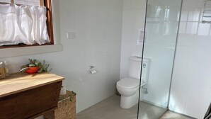 Uma casa de banho moderna com toucador de madeira, sanita e cabine de duche em vidro.