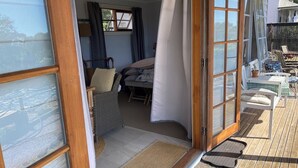 Quarto com porta de vidro deslizante que dá para um terraço externo. No interior, há uma cadeira de vime e uma cama com cabeceira branca.