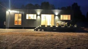 A single-story metal building with a porch and a small outdoor seating area. - Lakeside Off-Grid Luxury Cabin Redman View (Lake Fyans)