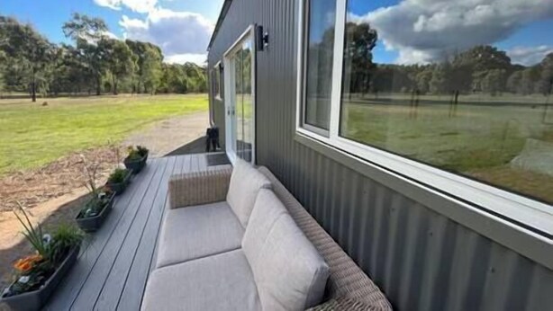 A modern outdoor seating area with a built-in bench and a view of a grassy field. - Lakeside Off-Grid Luxury Cabin Redman View (Lake Fyans)