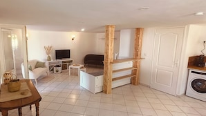 Un espacio habitable compacto con sofá, televisor, una pequeña mesa con una cesta, lavadora y estantería de madera.