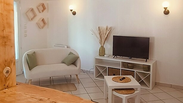 Una sala moderna con un banco de madera, un sofá blanco, un televisor sobre un mueble blanco y una mesita con un mantel tejido.