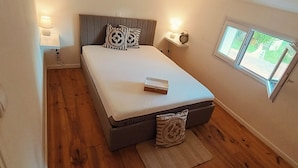 Un dormitorio con cama, lámparas de noche, mesita de noche, ventana y vistas al exterior.
