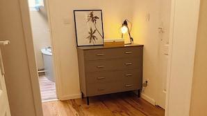 Un pasillo con suelo de madera, un aparador gris con cajones, un cuadro en la pared y una lámpara de pie.