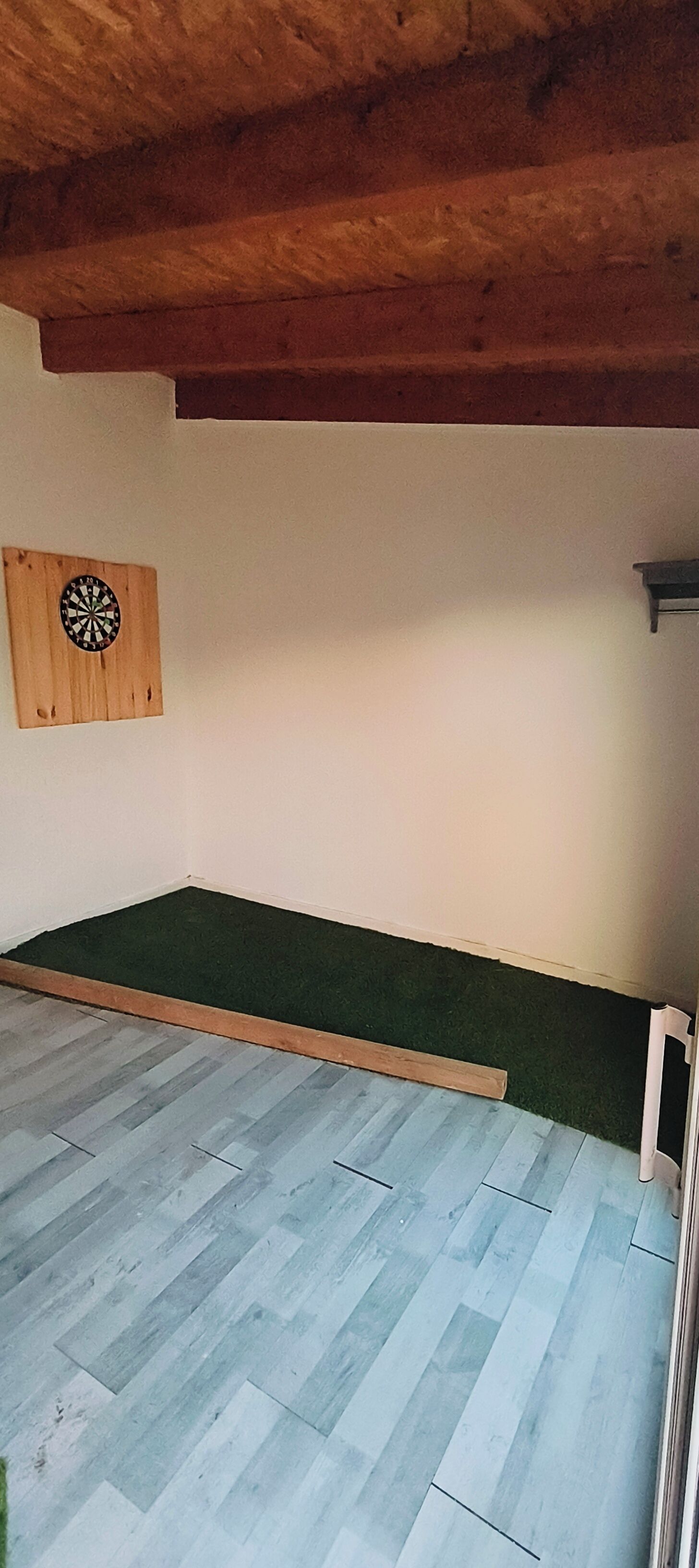 Una habitación con techo de madera, dardos y alfombra verde.