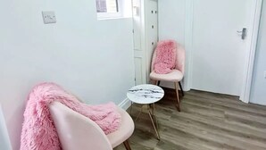 Una habitación con dos sillas rosadas, una mesita redonda pequeña y suelo de madera.
