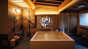 A modern bathroom with a large bathtub, a shower, and a wooden bench. - Sekitei (Hatsukaichi)