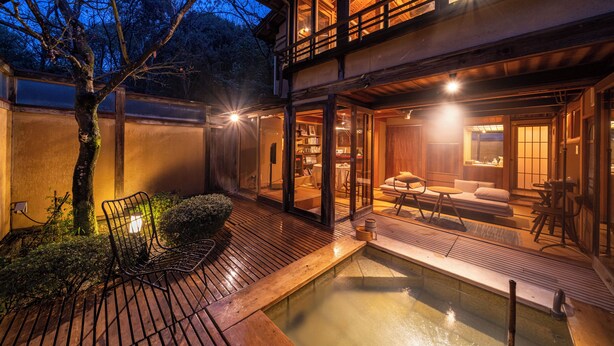 A traditional Japanese-style building with a wooden deck, a small pond, and a seating area with cushions and a low table. - Sekitei (Hatsukaichi)